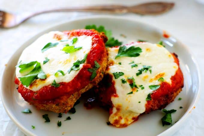 Two air fryer eggplant medallions topped with marinara and cheese on a white plate and fork in the background.