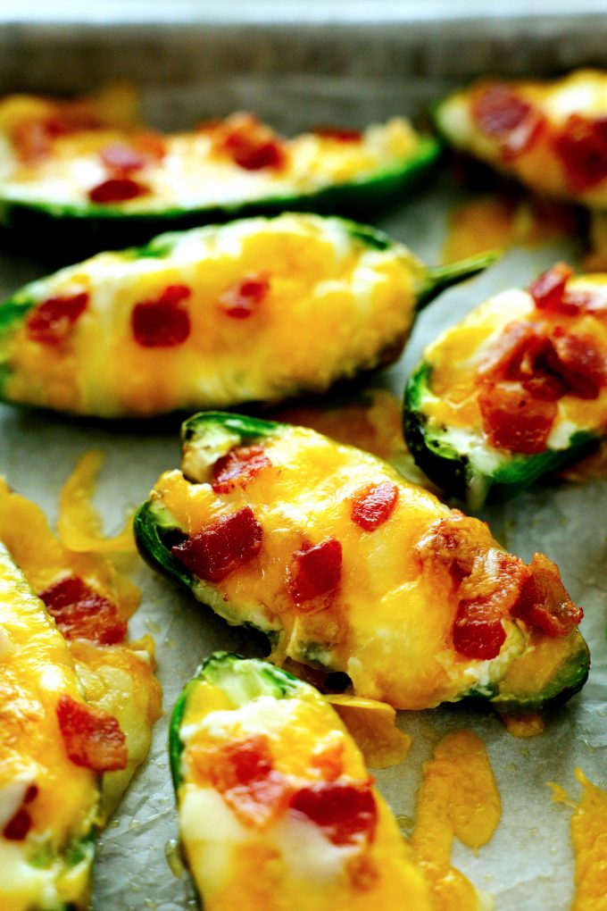 Baked Jalapeno Poppers topped with cheese and bacon on a sheet pan.