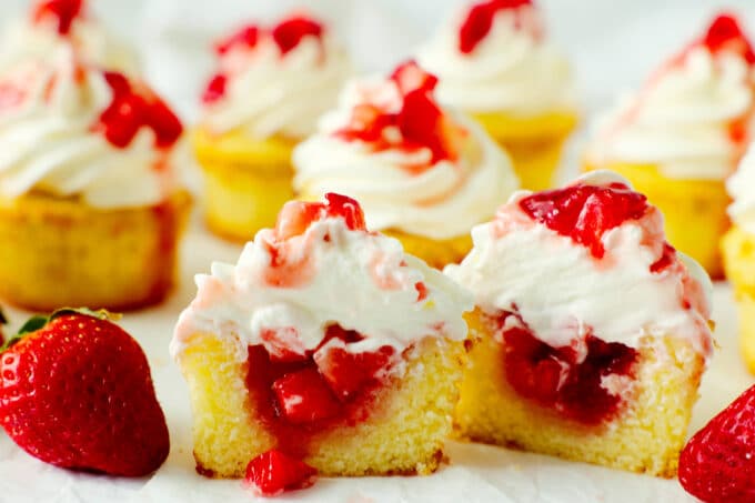 A group of strawberry shortcake cupcake cut in half with strawberries spilling out the center.
