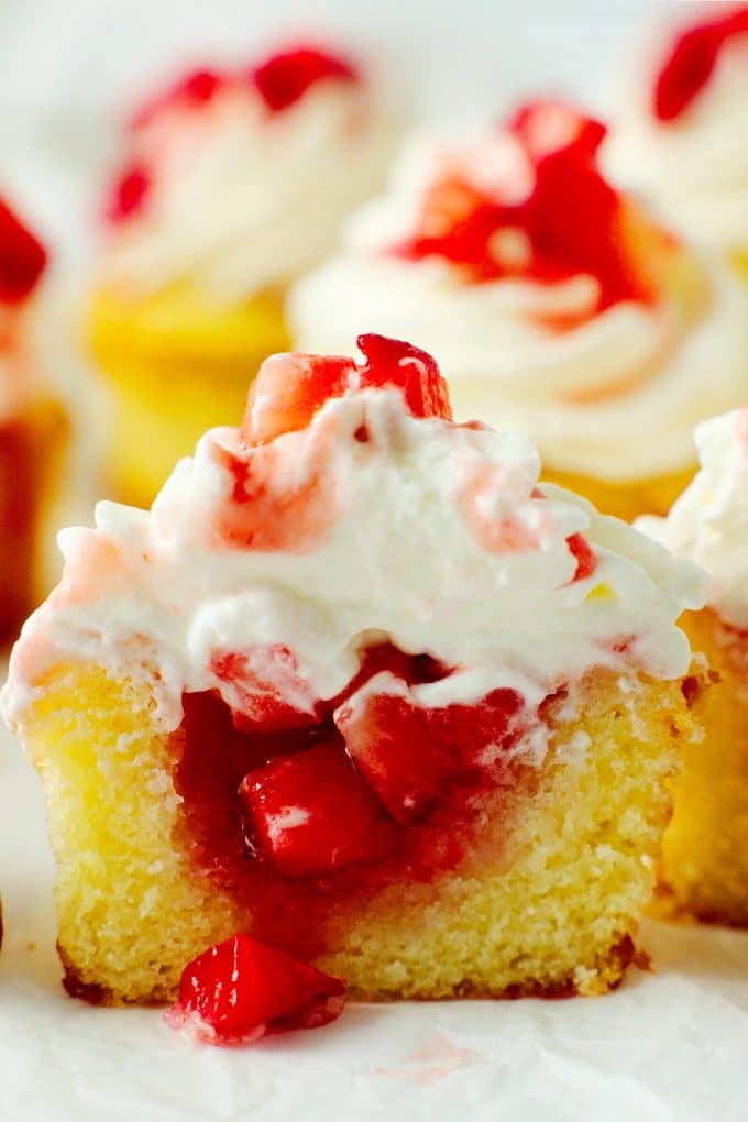 A close up shot of a strawberry shortcake cupcake cut in half with strawberries spilling out the center.