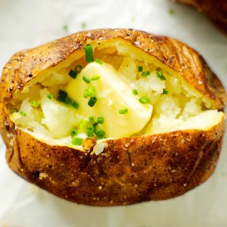 An overhead shot of an air fryer baked potato with a pad of butter and chives inside.