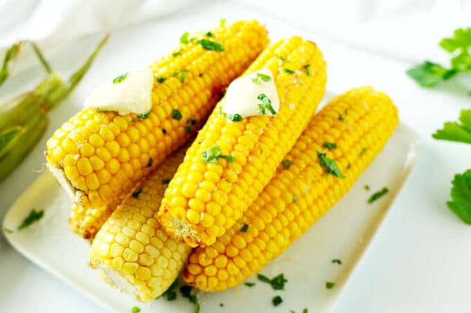 Air Fryer Corn On the Cob with butter pads on top of them stacked on a white plate.