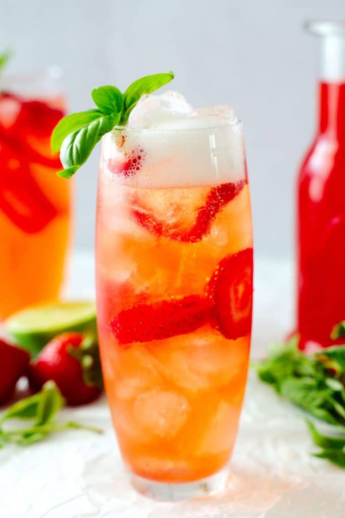 A close up shot of a strawberry basil cocktail with fizz at the top of the glass and a basil garnish.