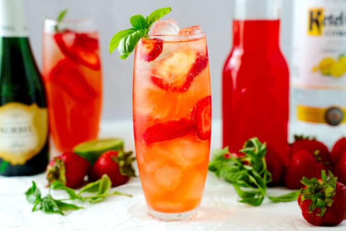 Strawberry Basil Cocktail with simple syrup, vodka, and champagne in the background.