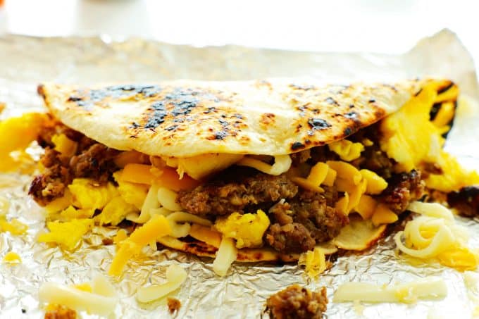 A sausage egg and cheese breakfast taco folded over on top of a sheet of aluminum foil.