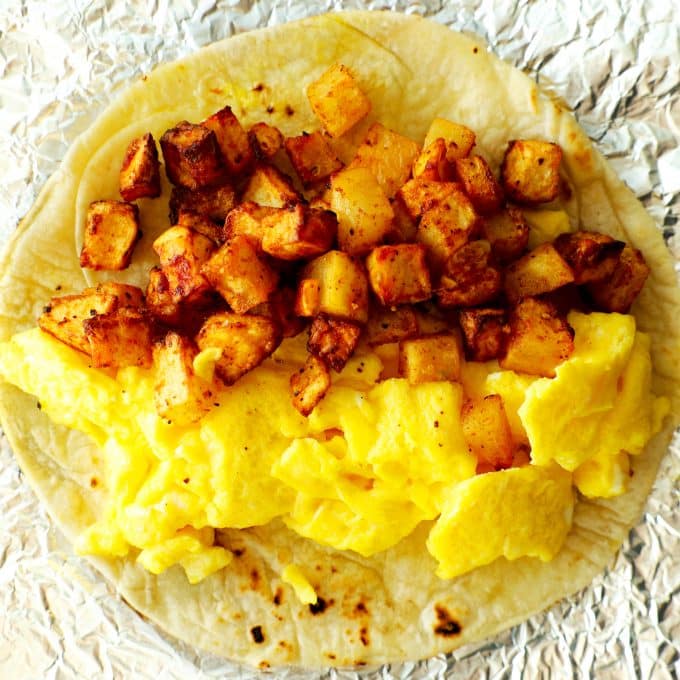 A tortilla with hashbrown potatoes and scrambled eggs inside.