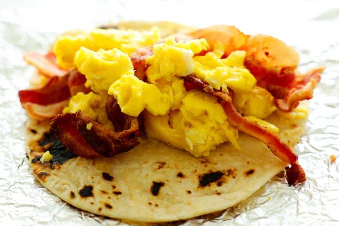 A tortilla with scrambled eggs and strips of bacon inside.
