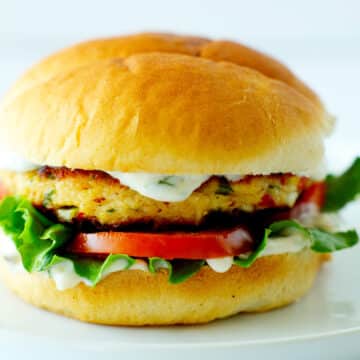 A crab cake sandwich with vegetables and tartar sauce on a white plate.