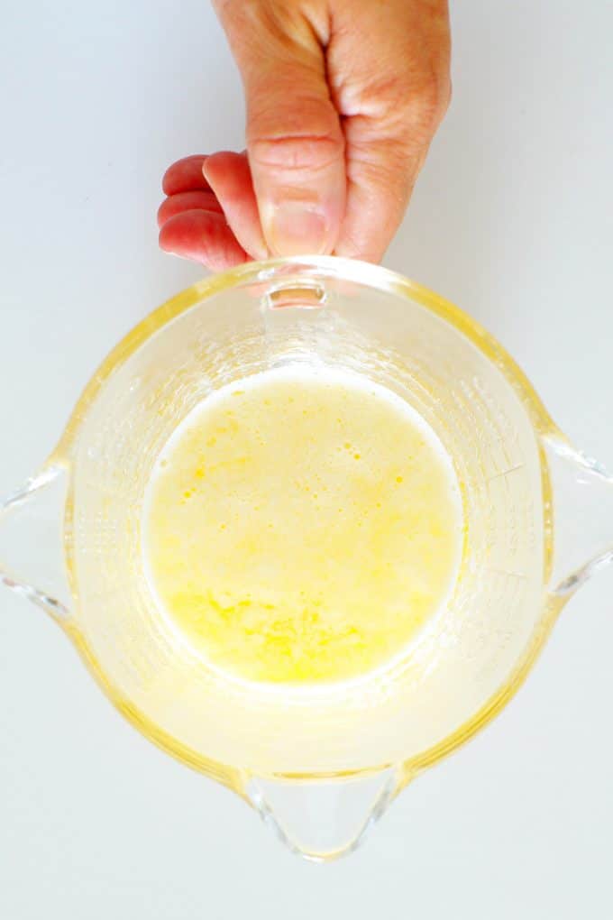 Melted butter in a measuring pitcher with a hand holding the handle.