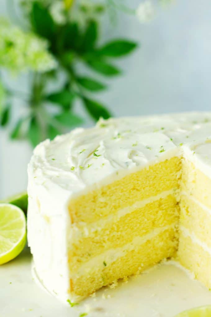 Key lime cake on a cake stand with a slice cut out of it.
