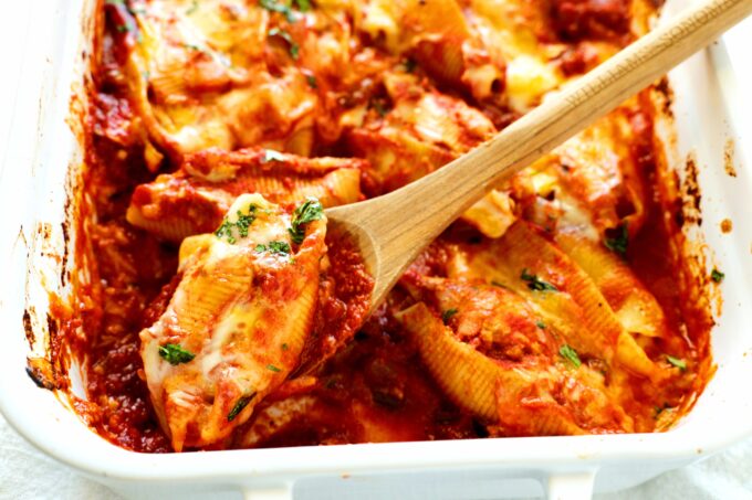 Mexican stuffed shells and a white casserole dish with a wooden spoon scooping out a shell.