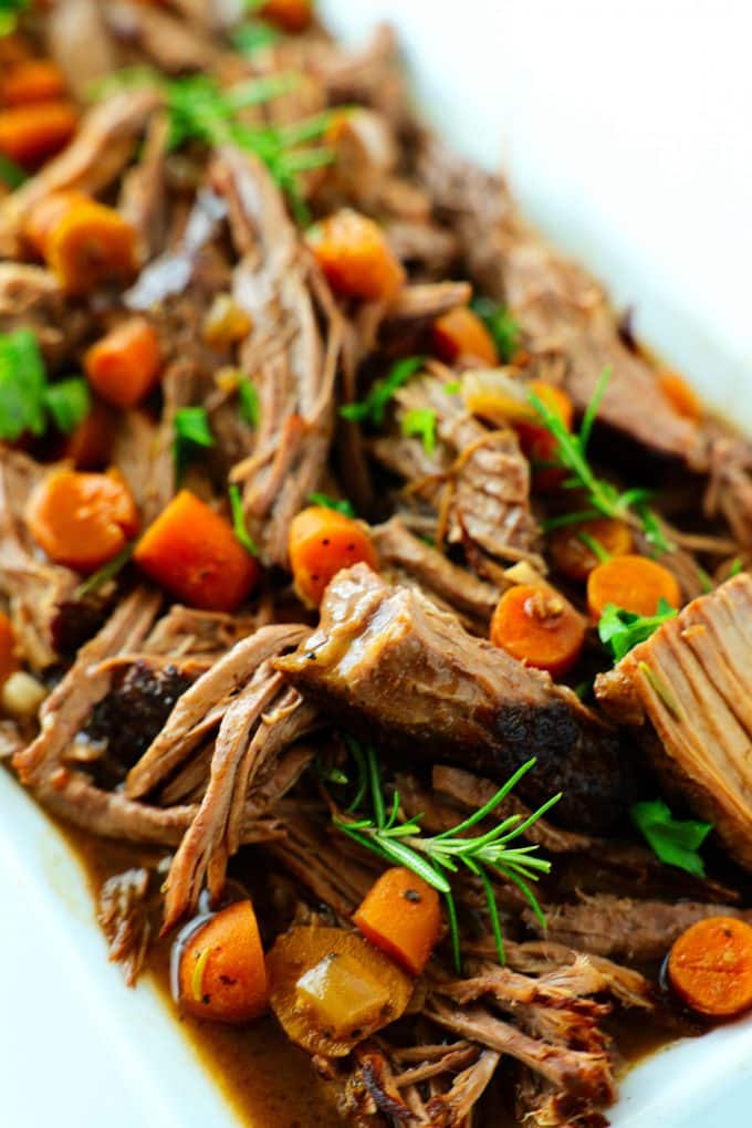 Slow cooker rump roast with carrots and rosemary on a white platter.