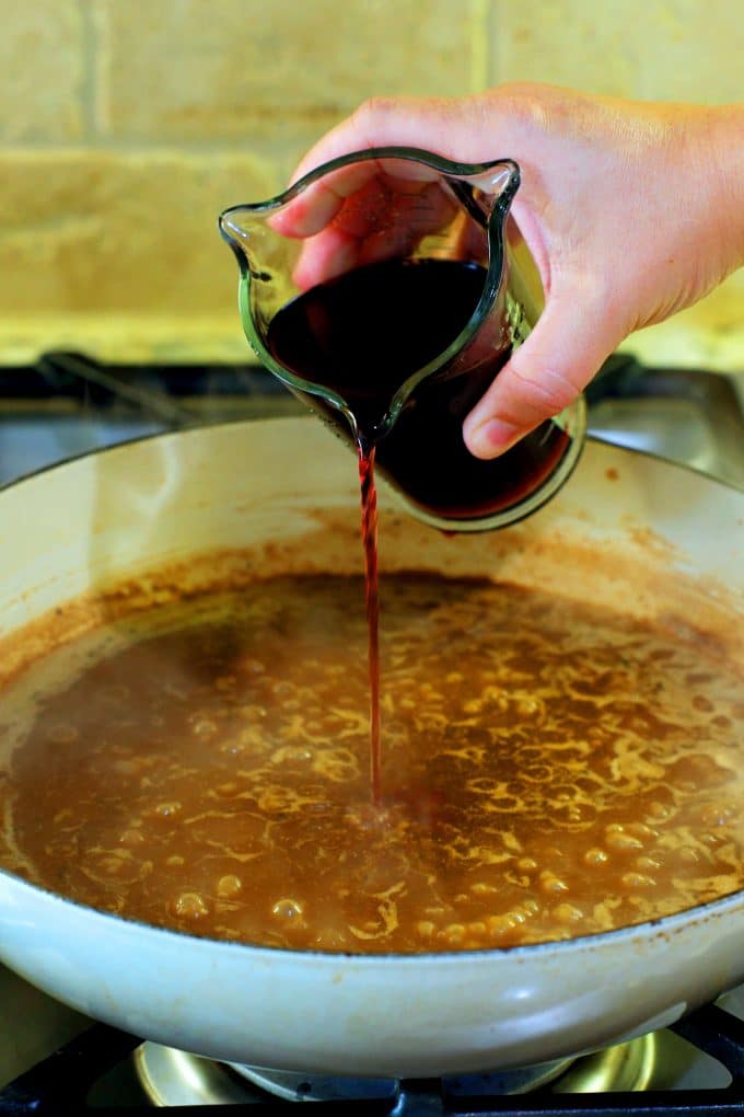 Wine being poured into a gravy on the stovetop.