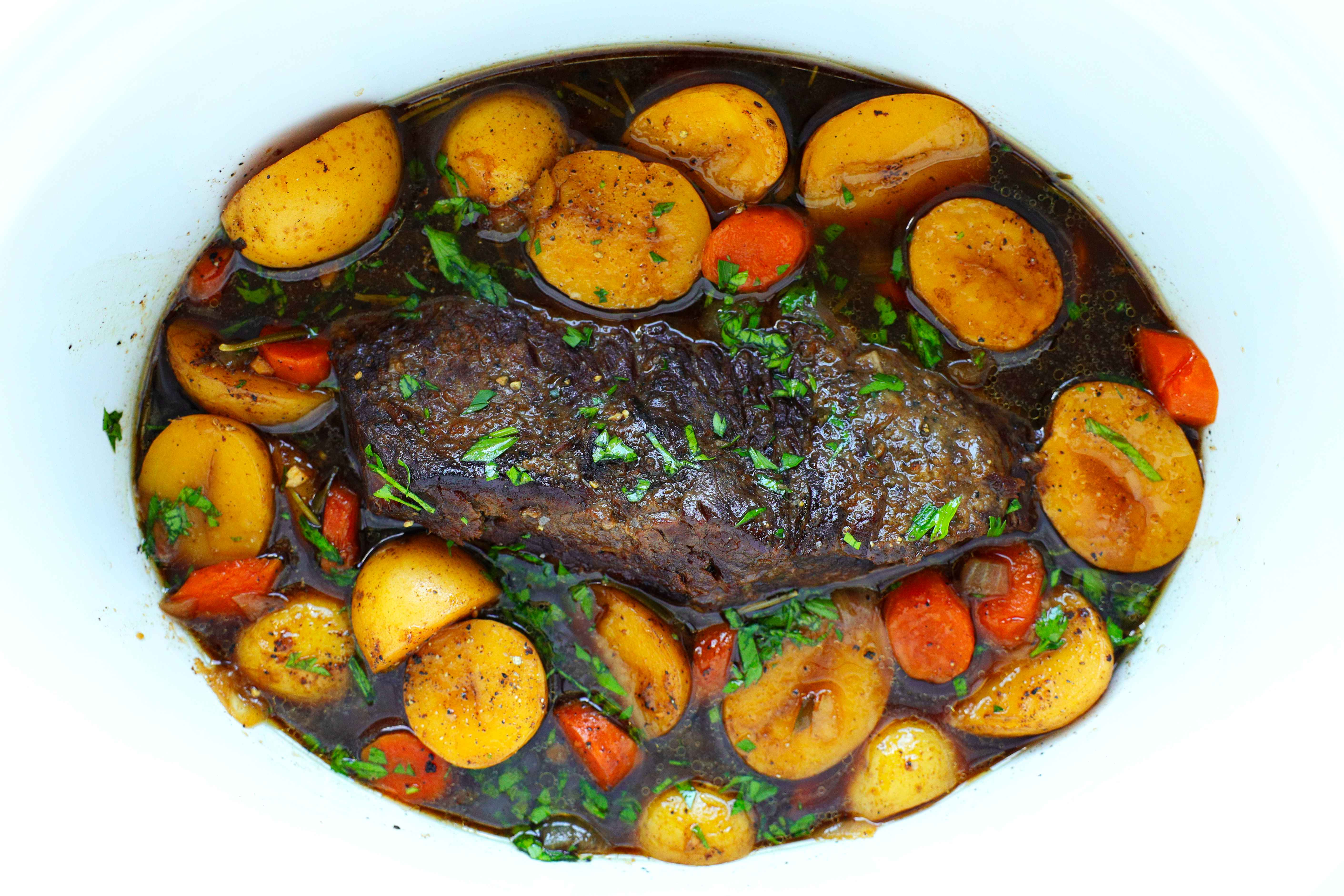 Rump roast in a slow cooker with veggies, gravy, and fresh rosemary