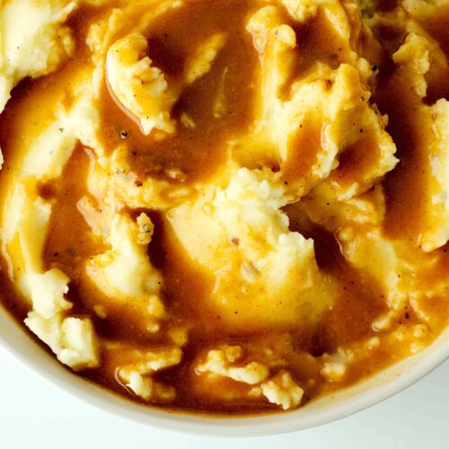 An overhead shot of brown beef gravy on mashed potatoes in a bowl.