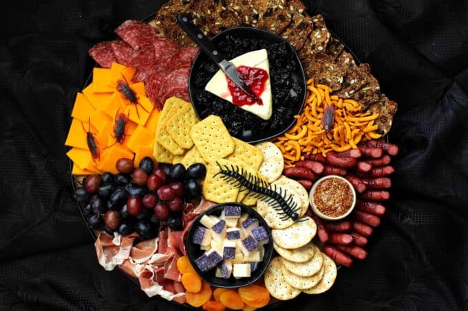 Halloween charcuterie board on a round platter with bugs crawling on top of it sitting on a black surface.