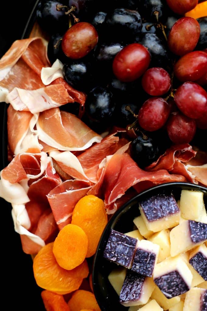 A close-up shot of prosciutto, dried apricots, and cubes of Merlot cheese