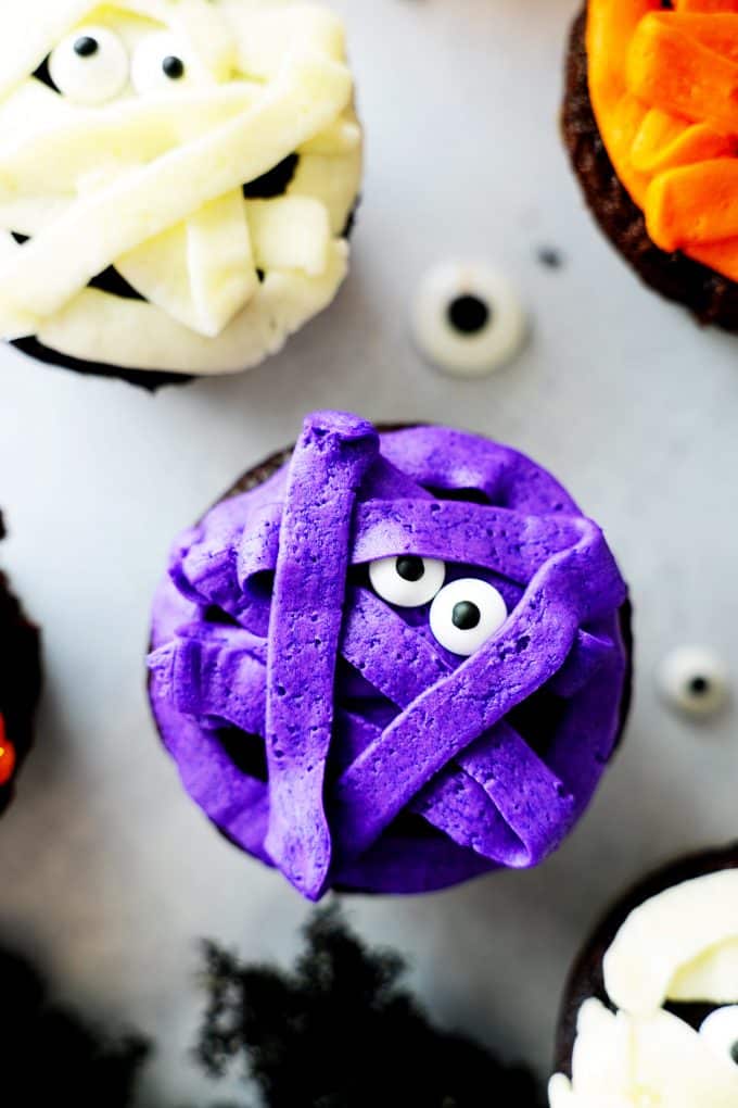 A mummy cupcake on a white surface with purple frosting.