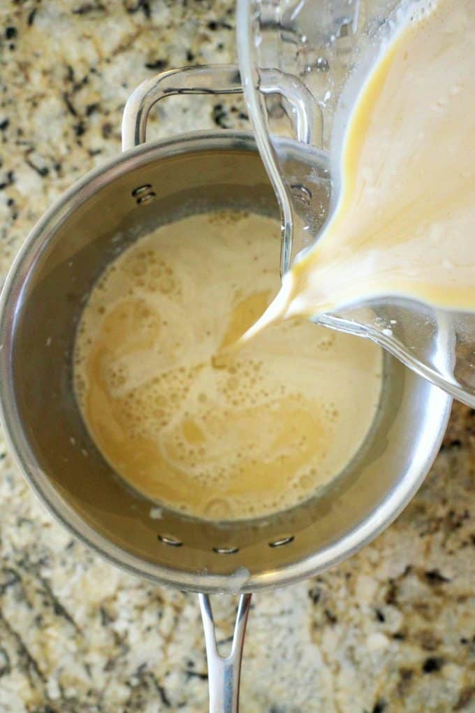 A pudding mixture being poured out of a mixing bowl into a sauce pan.