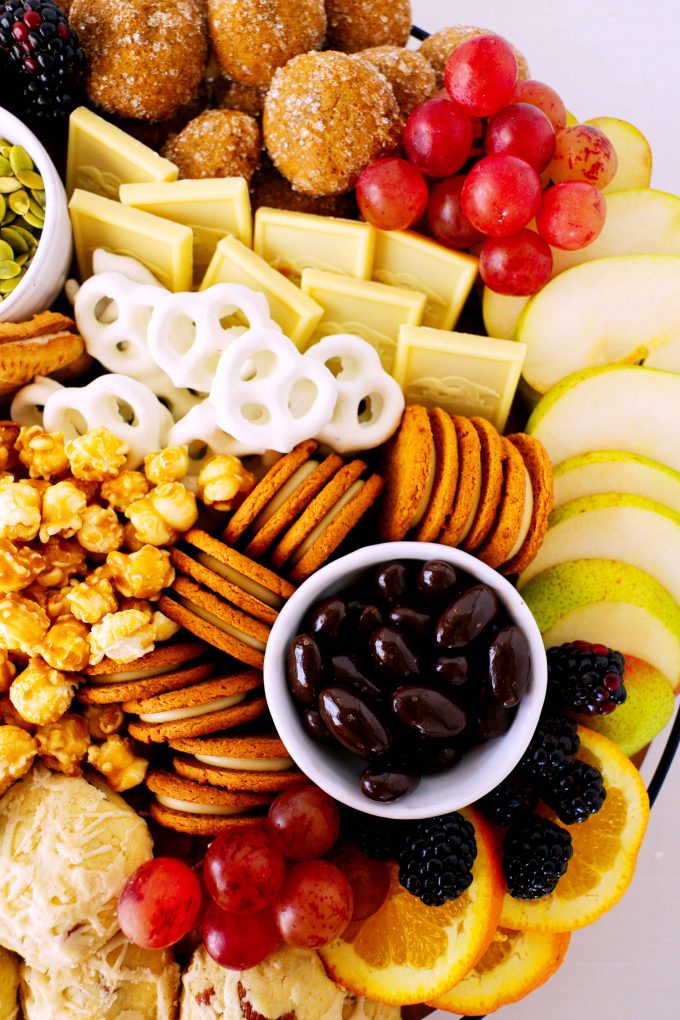 And overhead shot of chocolate covered almonds surrounded by fruit and cookies on a desert charcuterie board.