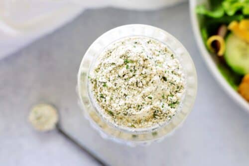 And overhead shot of ranch dressing mix in a bottle with a spoon and a salad off to the side.