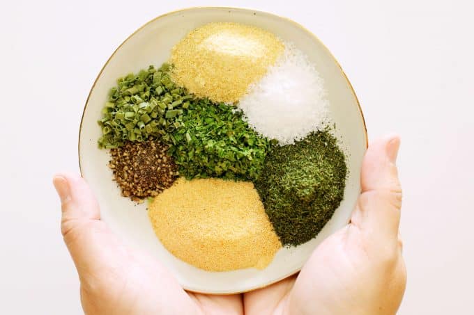 All of the different herbs and dried spices that go into ranch dressing mix on a plate.