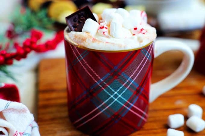 Hot chocolate in a mug on a wooden surface with marshmallows off to the side.