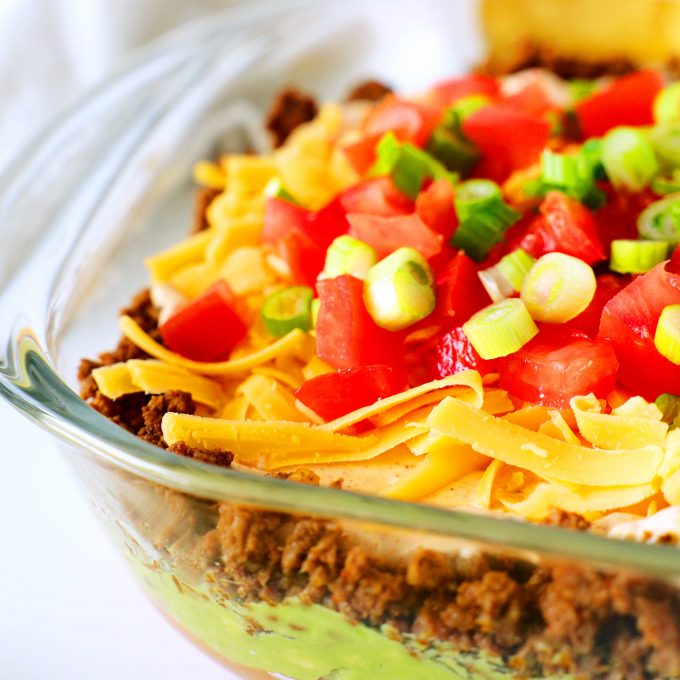 A close-up shot of seven layer taco dip in a clear glass baking dish.