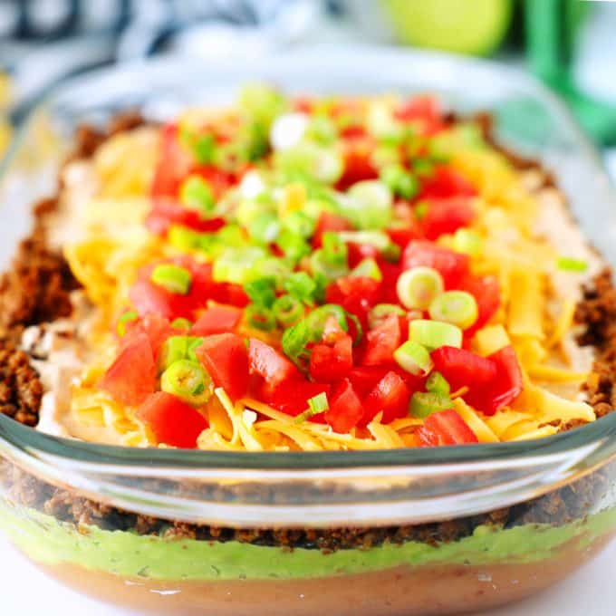 Seven layer taco dip with tomatoes and green onions on top.
