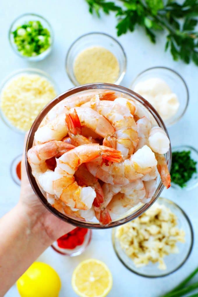 A bowl of shrimp being held over other bowls of ingredients