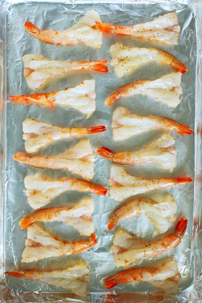 Butterflied shrimp laid out on a rimmed sheet pan.