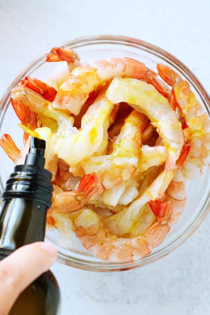Oil being drizzled over shrimp in a mixing bowl.