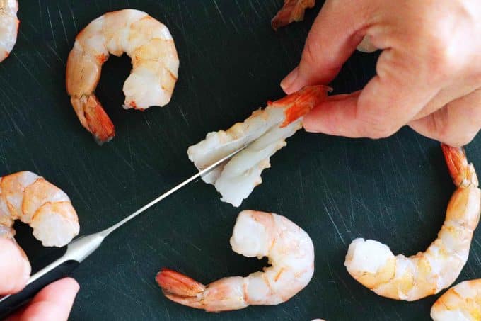A paring knife cutting into a shrimp in order to butterfly it.