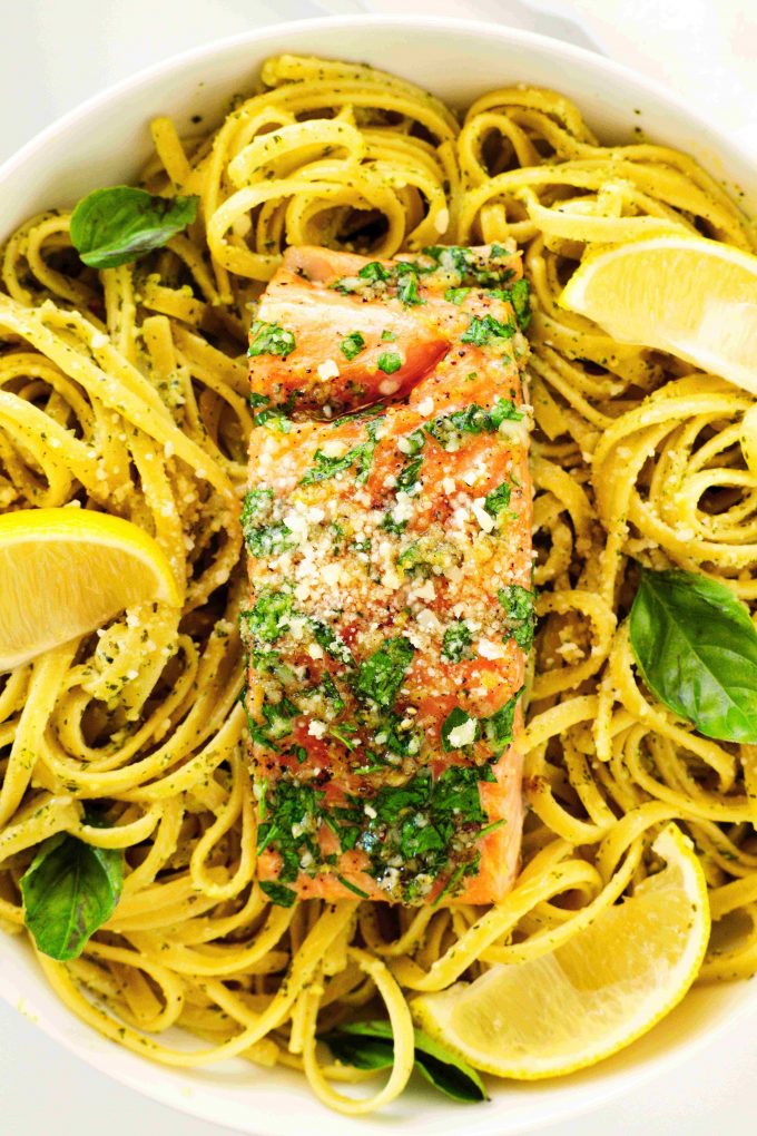 A close up shot of salmon pasta with a salmon fillet on top and lemon wedges all around it.