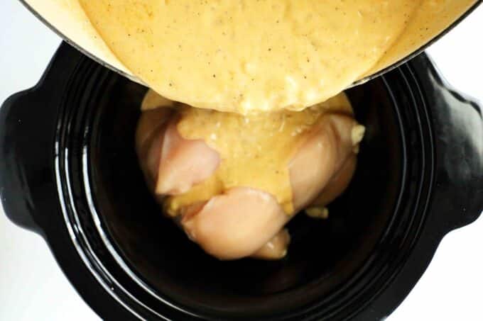 gravy being poured over chicken in crockpot