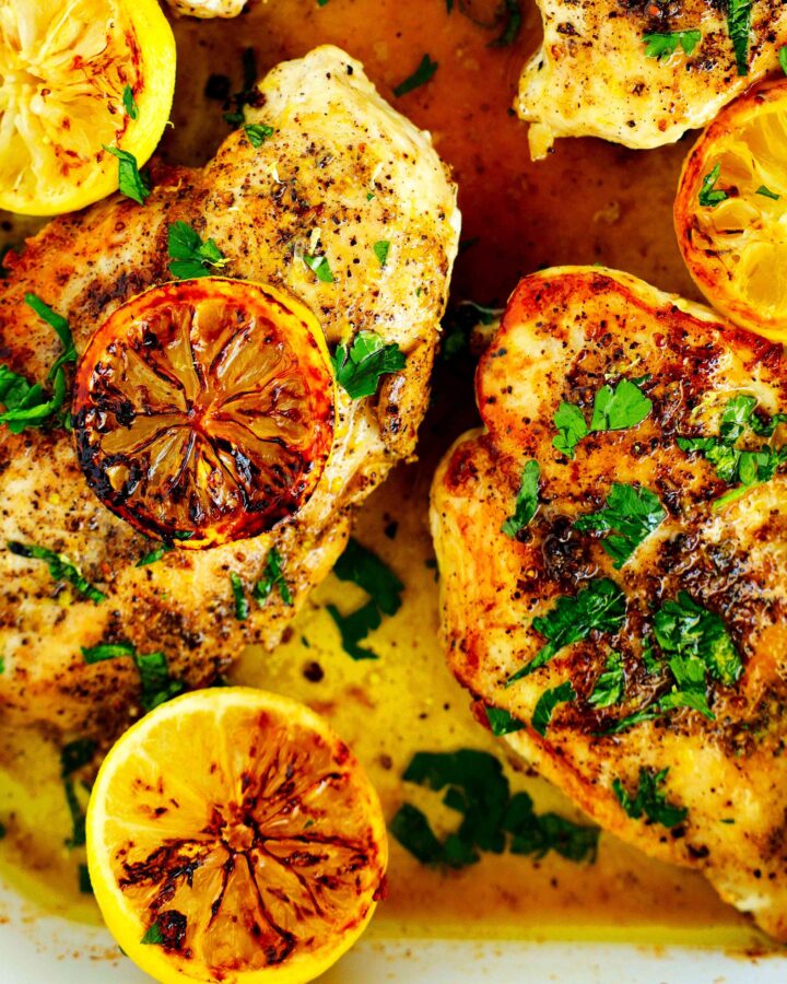 Two lemon pepper chicken breast in the corner of a baking dish with lemons surrounding it.