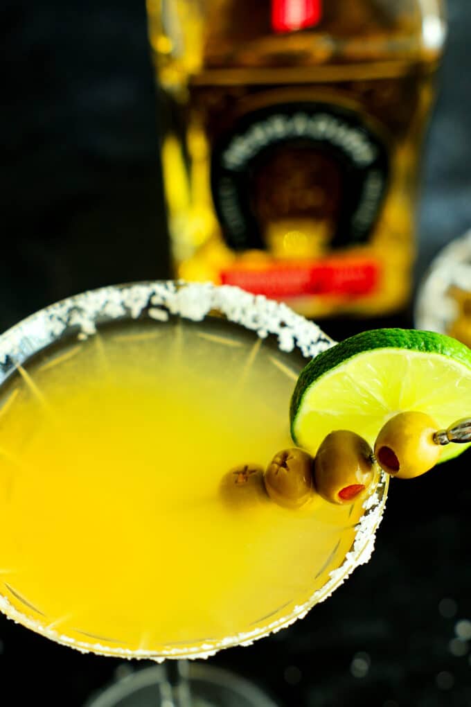 A close-up shot of a Mexican martini with a bottle of tequila in the background.