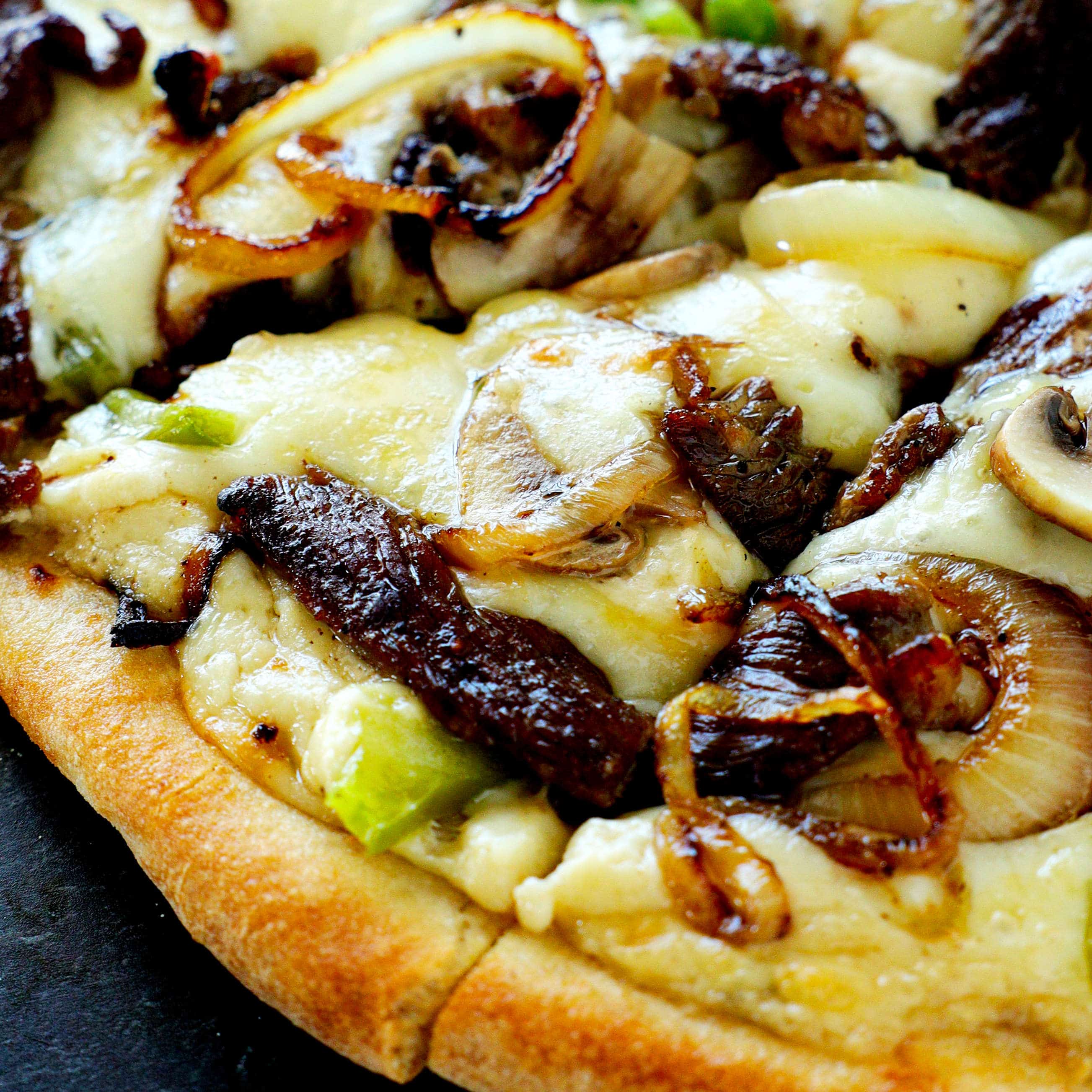 A close-up shot of a Philly cheesesteak pizza slice.