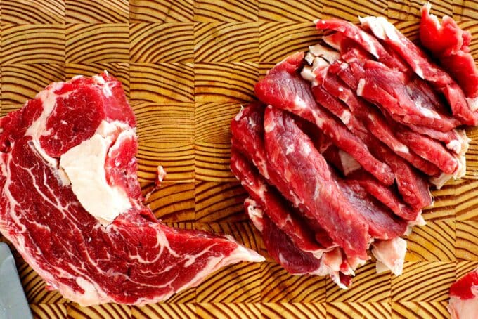 Ribeye steak on a cutting board cut into very thin slices.