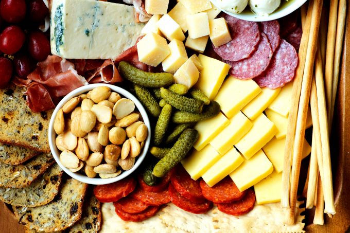 An overhead shot of a simple charcuterie board assembled with almonds, pickles, pepperoni, sliced cheese, meats, and crackers.