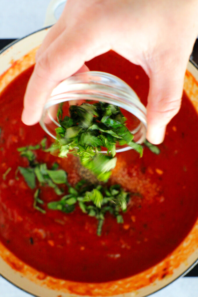 Basil being added to a pot of tomato sauce