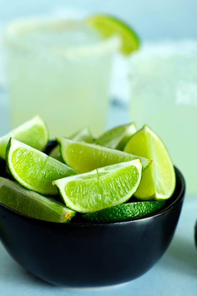 a bowl of lime wedges with margaritas in the background