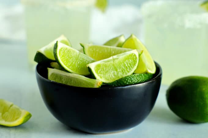 a bowl of lime wedges with margaritas in the background