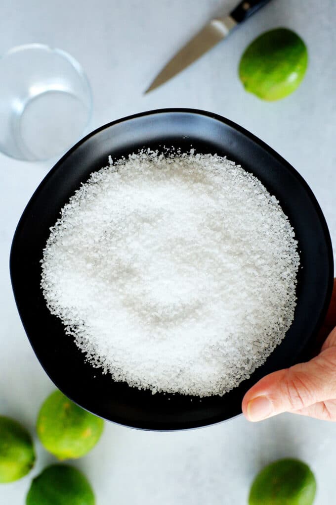 a hand holding a black bowl of kosher salt