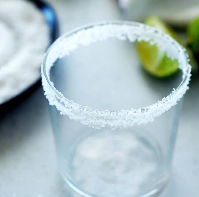 an empty glass with salt around the rim and limes in the background 
