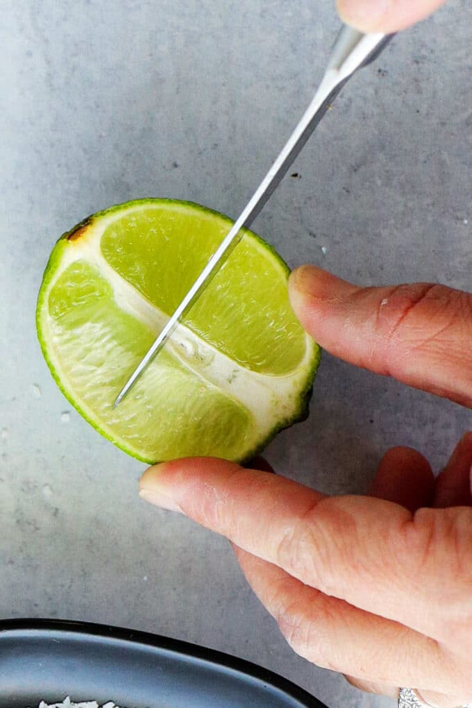 hands using a knife to cut across half of a lime