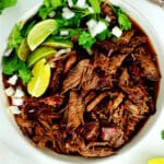 A bowl of beef birria stew with cilantro, lime, and onions on top
