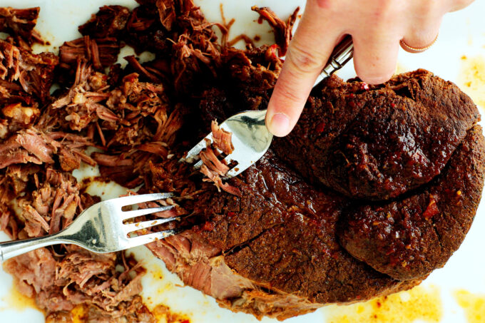 hands using forks to shred beef