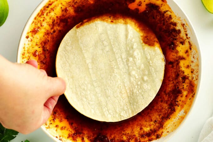A hand dipping a tortilla in birria grease