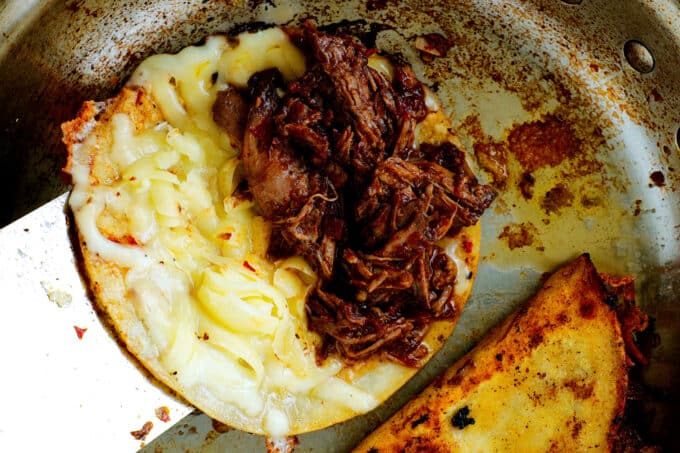 a tortilla in a pan with cheese on top and shredded beef on half of it
